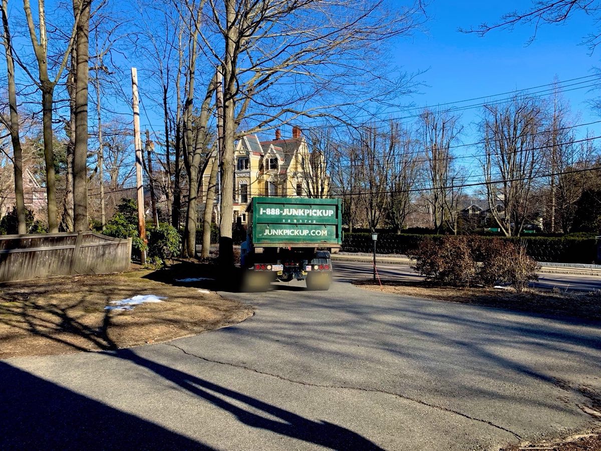 LPC Removal Service truck backing a JunkPickup.com roll-off dumpster into a driveway in Newton, MA